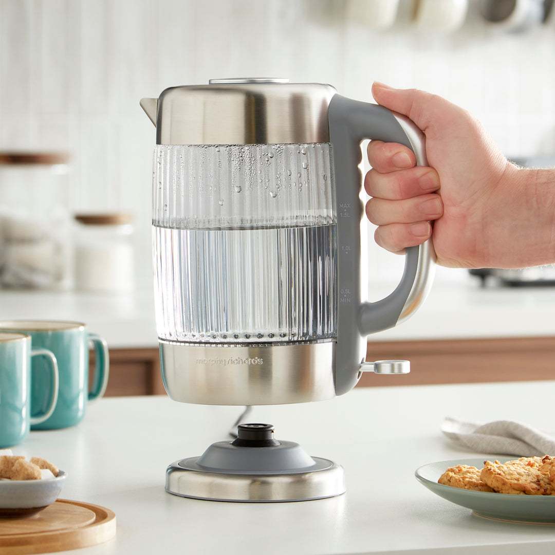 Person holding a stainless steel electric kettle on a kitchen counter.
