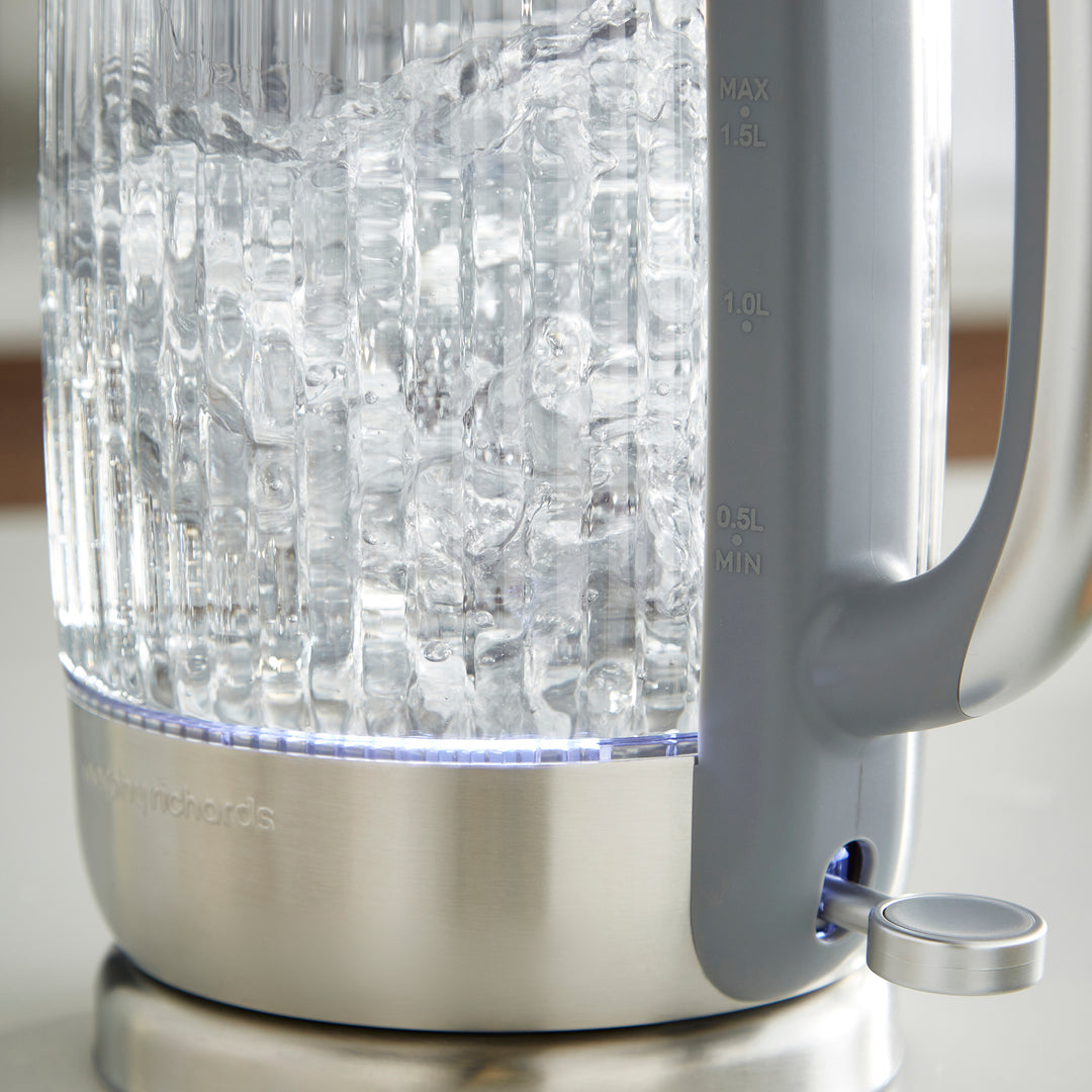 Clear glass electric kettle with ice cubes inside on a neutral background