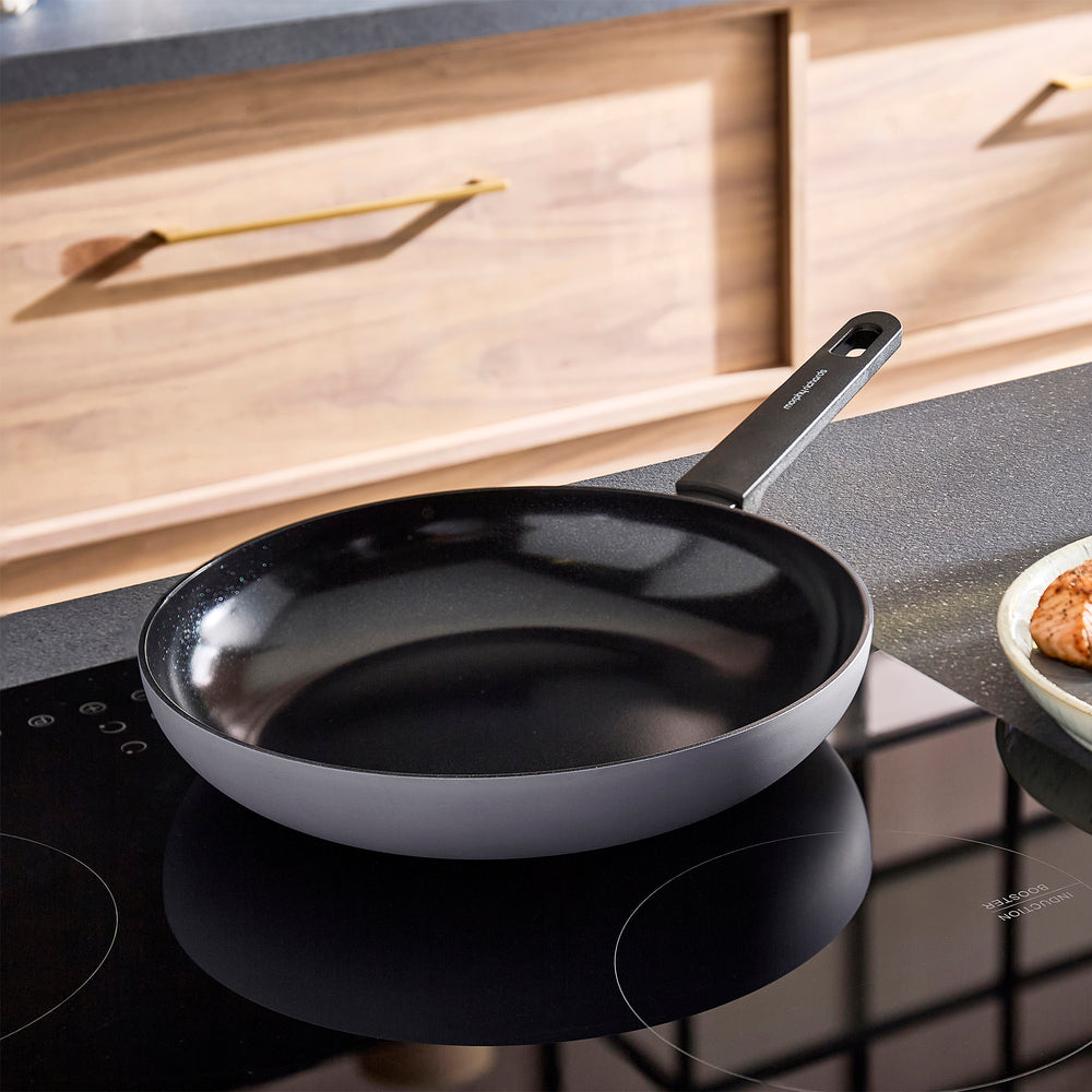 Black frying pan on a kitchen stove with a wooden cabinet in the background