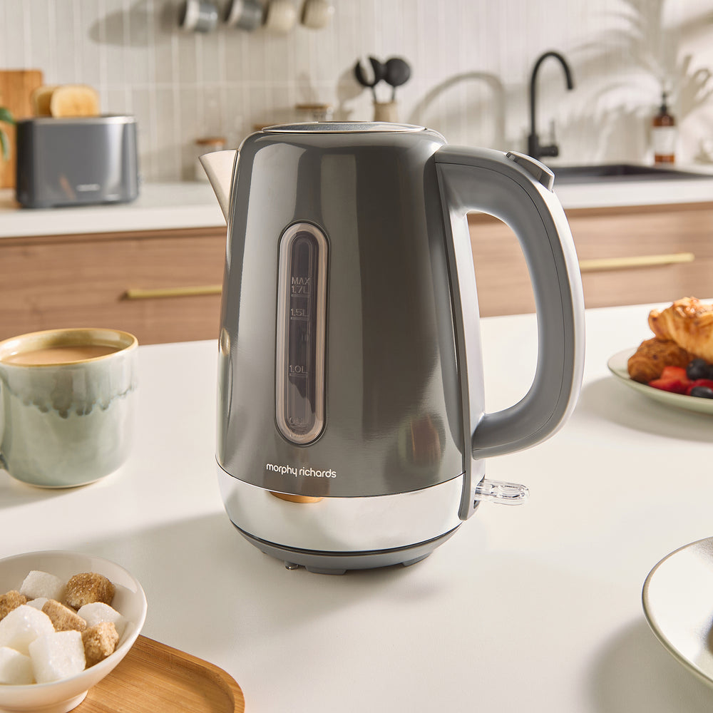 Grey electric kettle on a kitchen counter with a cup of coffee and snacks.